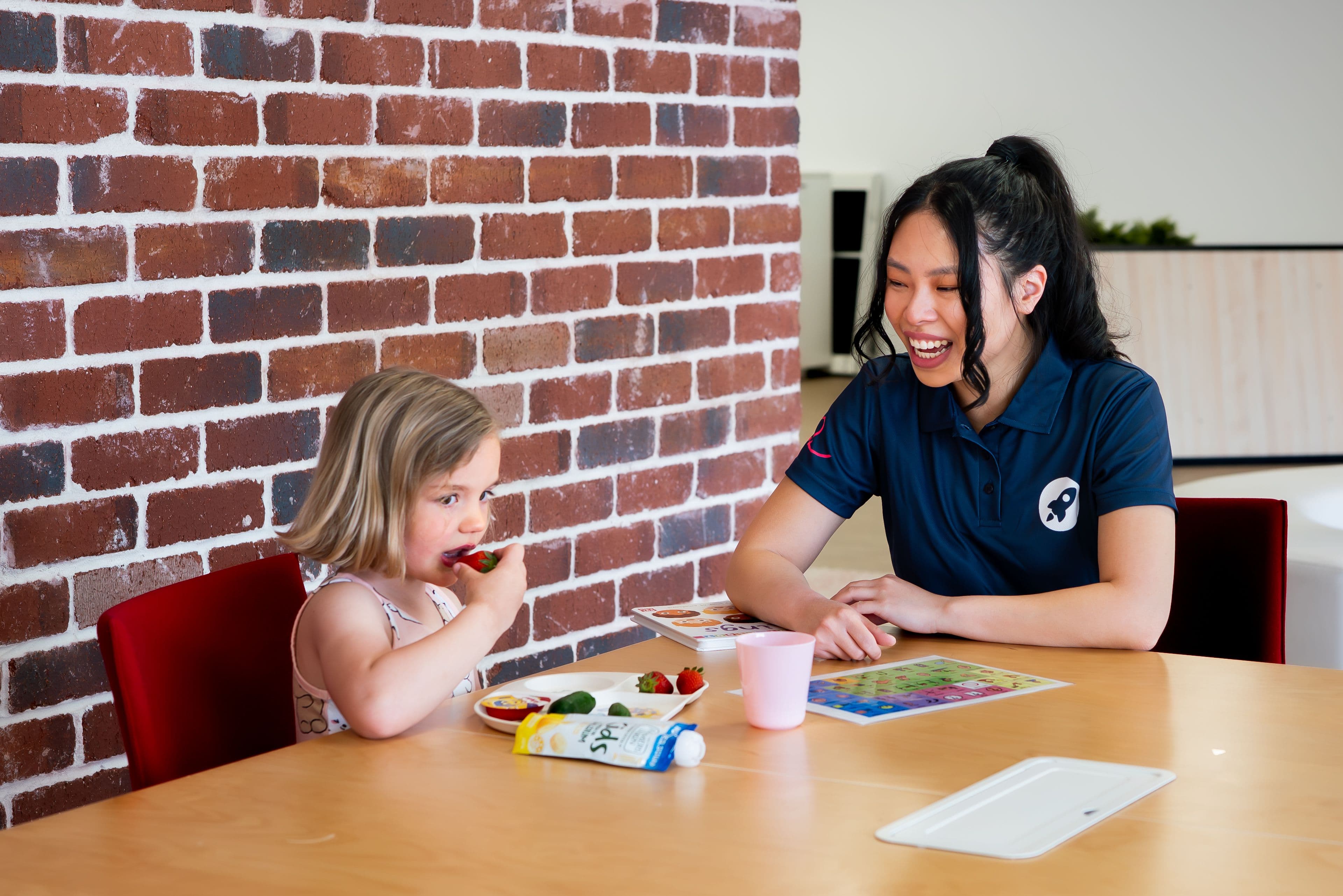 A clinician and a child at a table, the child is eating food