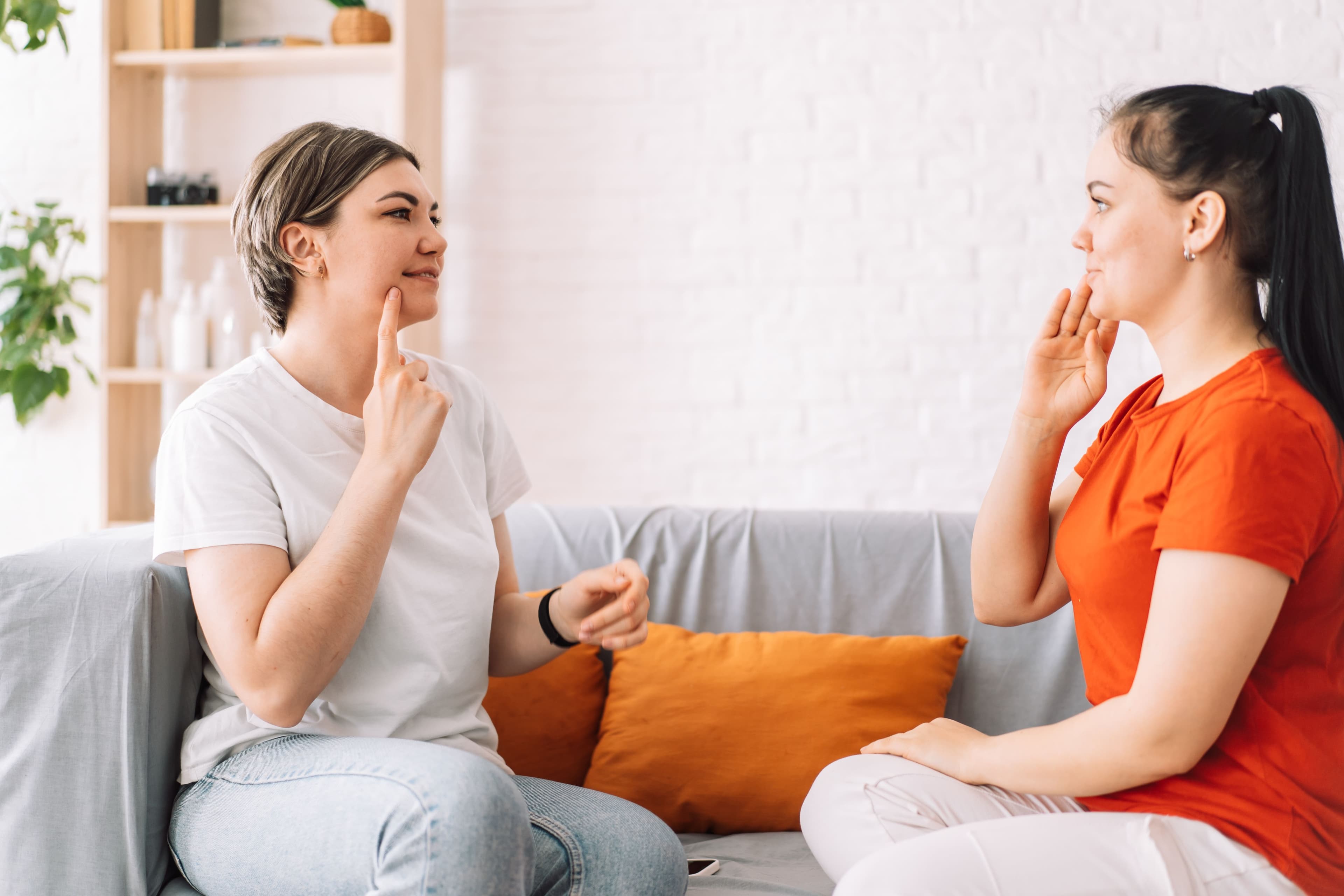 two women sitting on a sofa facing each other speaking in sign language