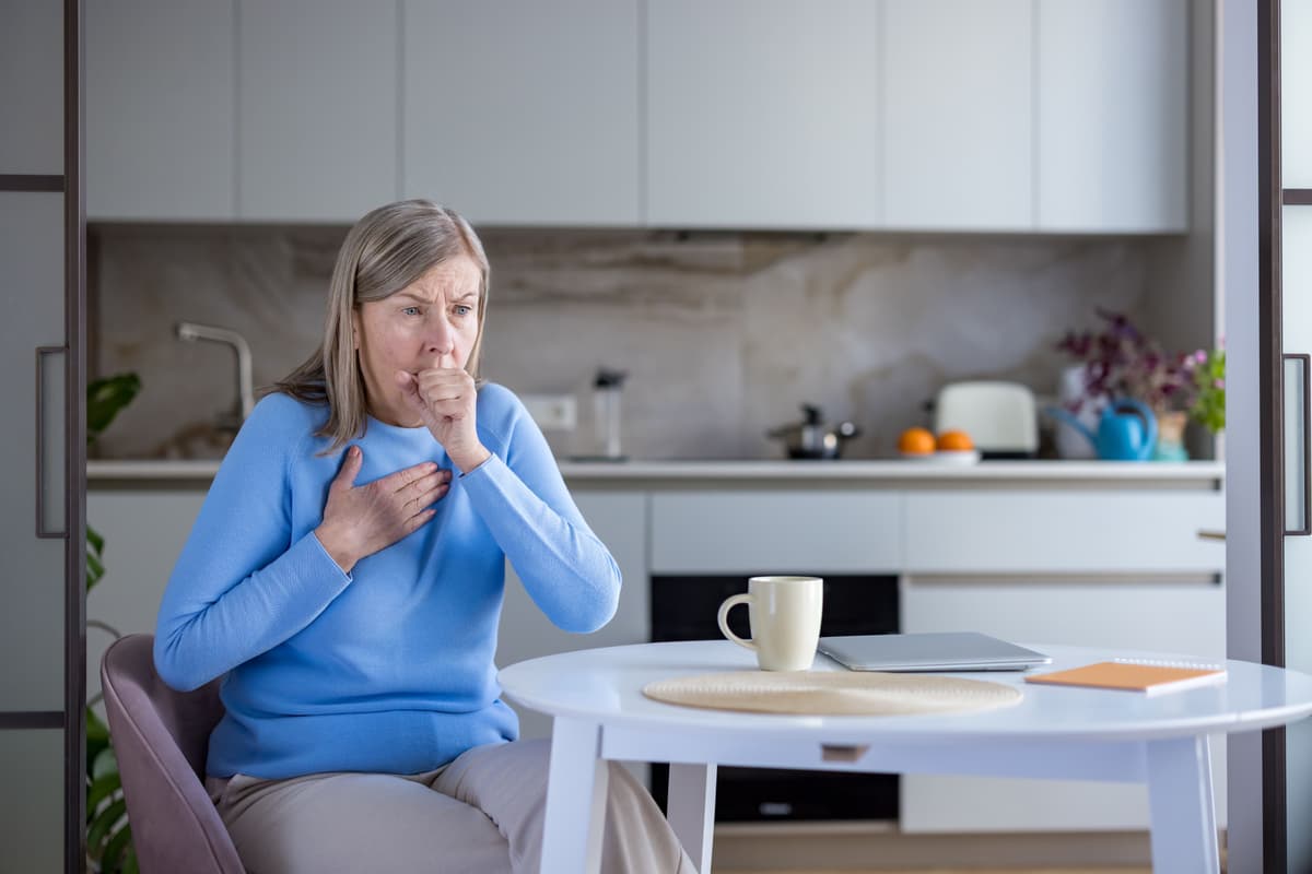 older woman coughing in a kitchen setting