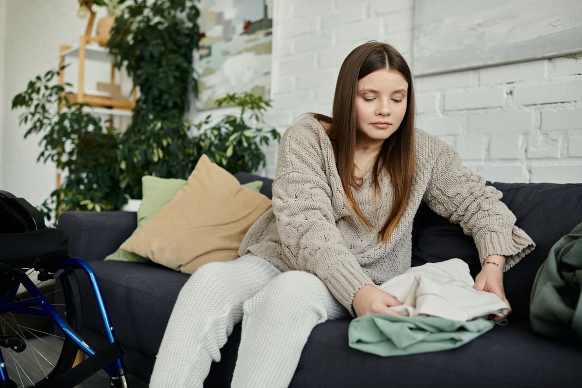woman sitting on couch folding clothes, with wheelchair nearby