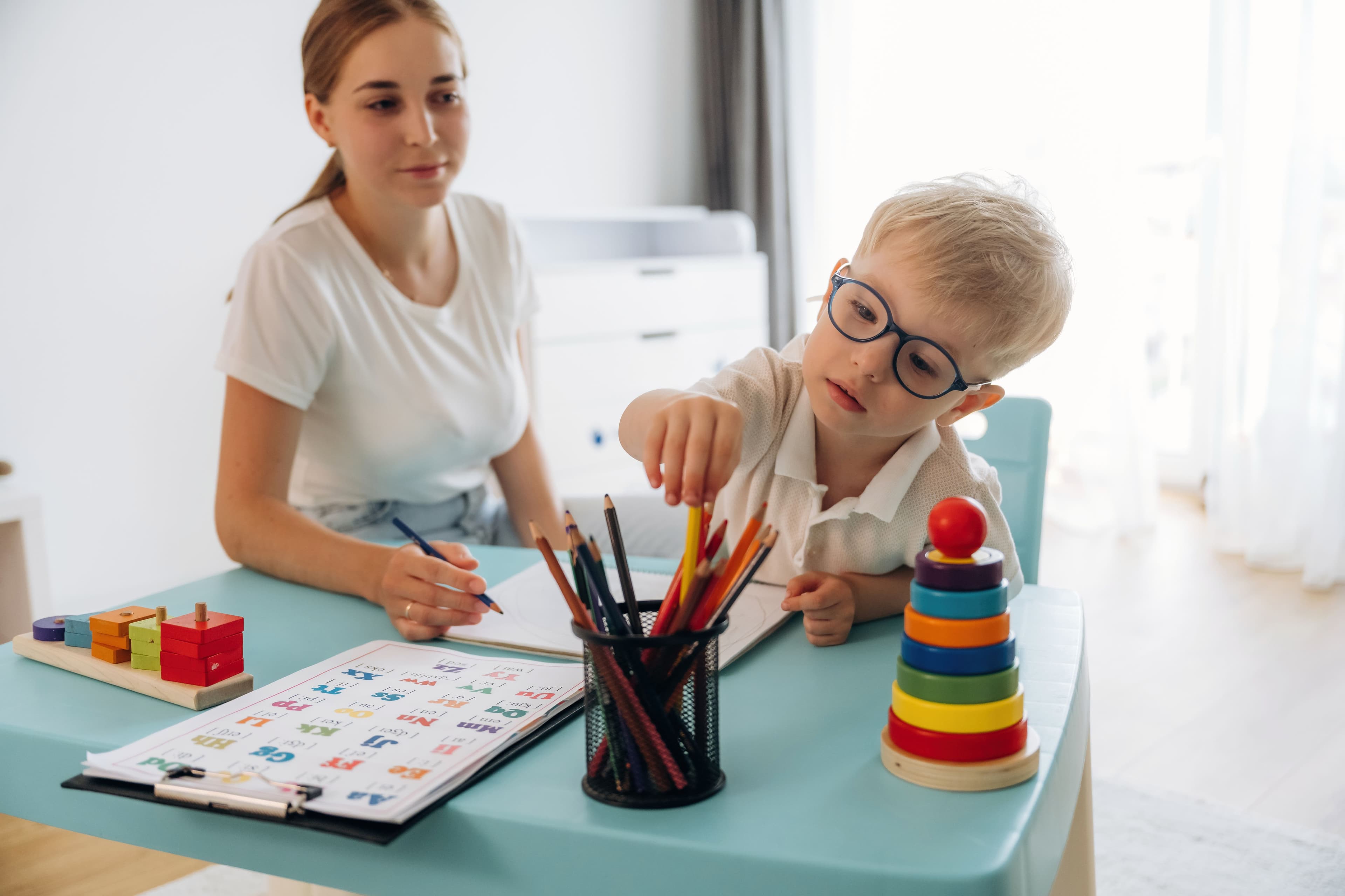 Boy Learning with Adult Supervision at Home, reaching for a pencil